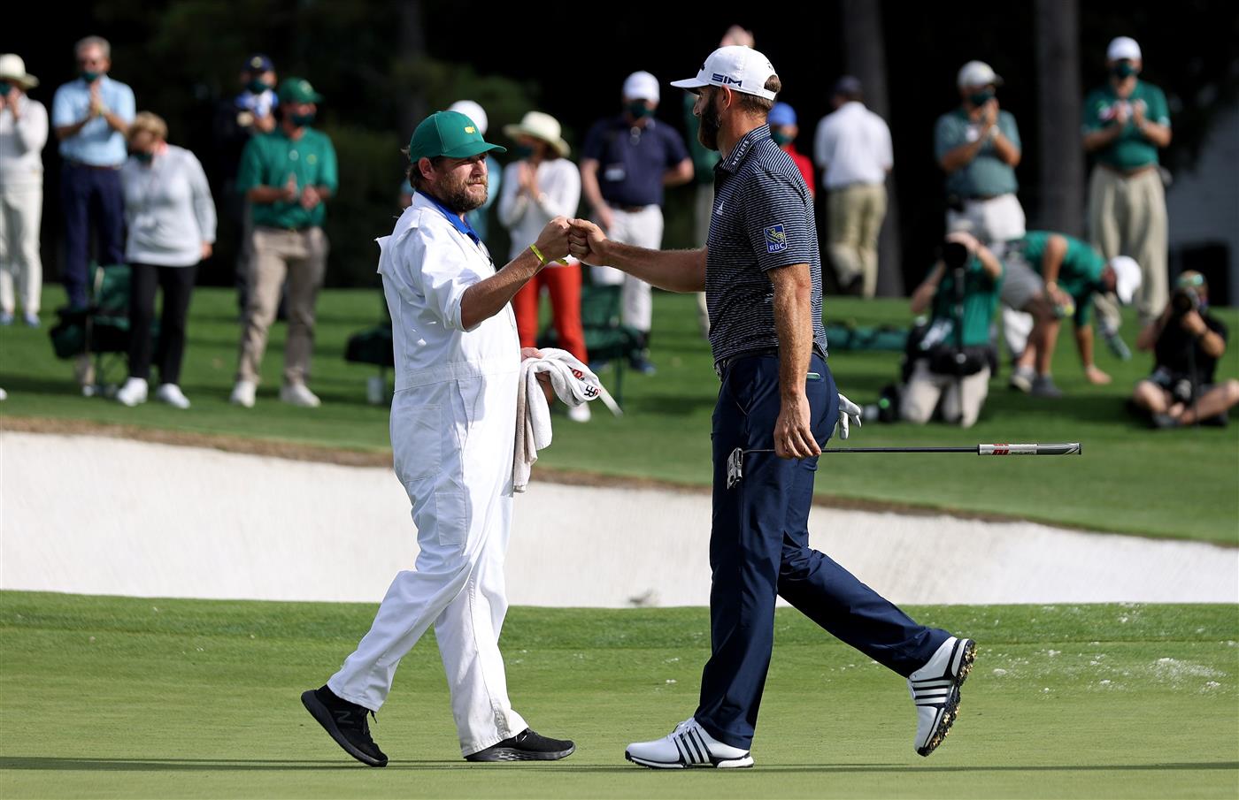 Dustin Johnson reacts with Dale Vallely, caddie for Abraham Ancer of Mexico (not pictured), on the 18th green after winning the Masters at Augusta National Golf Club (Photo by Getty Images)