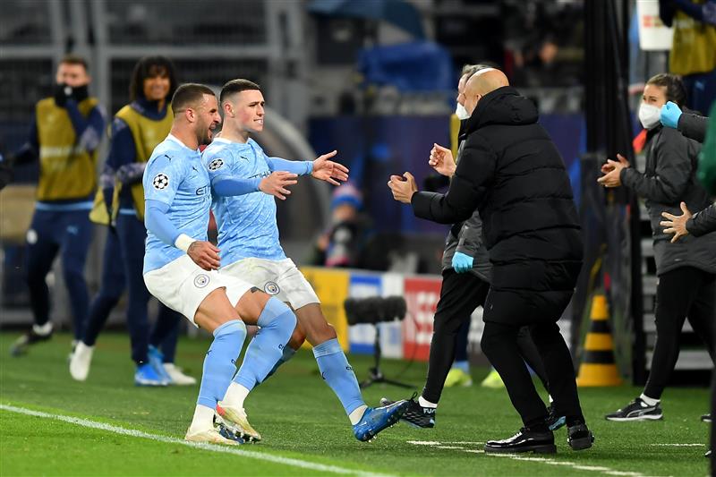 DORTMUND, GERMANY - APRIL 14: Phil Foden of Manchester City runs towards Pep Guardiola, Manager of Manchester City as he celebrates with team mate Kyle Walker (L) after scoring their side's second goal during the UEFA Champions League Quarter Final Second Leg match between Borussia Dortmund and Manchester City at Signal Iduna Park on April 14, 2021 in Dortmund, Germany. Sporting stadiums around Germany remain under strict restrictions due to the Coronavirus Pandemic as Government social distancing laws prohibit fans inside venues resulting in games being played behind closed doors.  (Photo by Frederic Scheidemann/Getty Images)