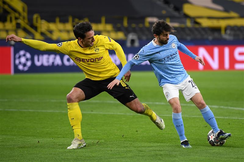 DORTMUND, GERMANY - APRIL 14: Bernardo Silva of Manchester City is challenged by Mats Hummels of Borussia Dortmund during the UEFA Champions League Quarter Final Second Leg match between Borussia Dortmund and Manchester City at Signal Iduna Park on April 14, 2021 in Dortmund, Germany. Sporting stadiums around Germany remain under strict restrictions due to the Coronavirus Pandemic as Government social distancing laws prohibit fans inside venues resulting in games being played behind closed doors.  (Photo by Frederic Scheidemann/Getty Images)