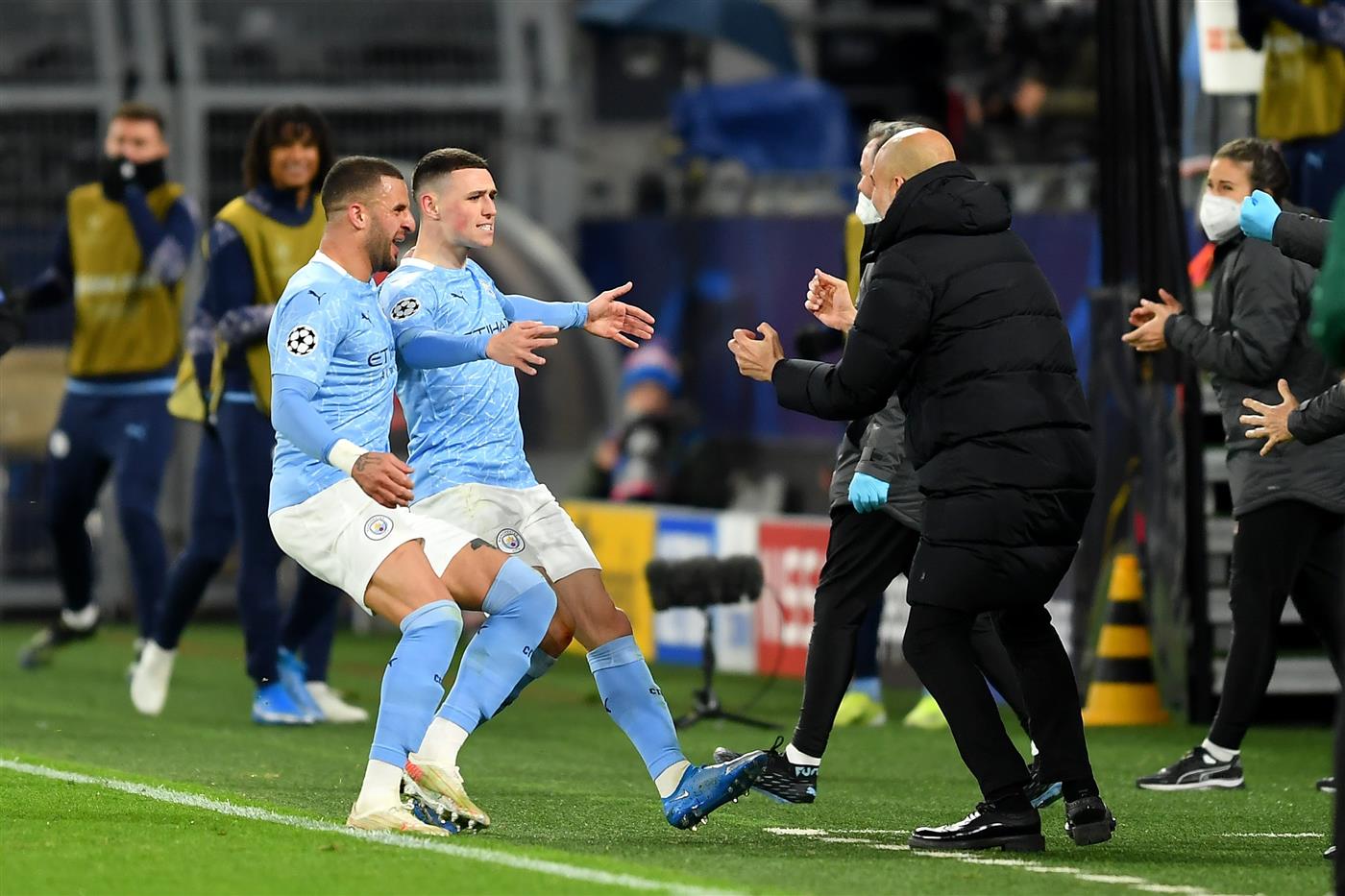 DORTMUND, GERMANY - APRIL 14: Phil Foden of Manchester City runs towards Pep Guardiola, Manager of Manchester City as he celebrates with team mate Kyle Walker (L) after scoring their side's second goal during the UEFA Champions League Quarter Final Second Leg match between Borussia Dortmund and Manchester City at Signal Iduna Park on April 14, 2021 in Dortmund, Germany. Sporting stadiums around Germany remain under strict restrictions due to the Coronavirus Pandemic as Government social distancing laws prohibit fans inside venues resulting in games being played behind closed doors.  (Photo by Frederic Scheidemann/Getty Images)