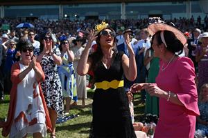 Racegoers react in the summer sunshine as a race finishes on the third day, known as the Lady