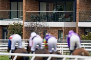 NEWBURY, ENGLAND - MARCH 04: Runner in the The Bet In-Running On Racing At BetVictor Veterans' Handicap Chase pass apartments as a gentleman watches from his lounge at Newbury Racecourse on March 04, 2023 in Newbury, England. (Photo by Alan Crowhurst/Getty Images)