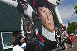 Racegoers pass a large mural of legendary jockey Frankie Dettori as they arrive on the second day of the Epsom Derby Festival horse racing event in Surrey, southern England on June 3, 2023. (Photo by JUSTIN TALLIS / AFP) (Photo by JUSTIN TALLIS/AFP via Getty Images)