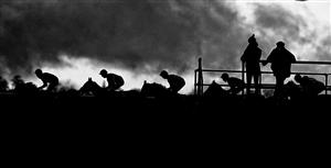 WINCANTON, ENGLAND - DECEMBER 03: (EDITORS NOTE: This image was processed using digital filters) Two stable staff look on as the runners in The Free Entry With Racing TV Club Days 'Junior' Standard Open NH Flat Race pass the grandstands at Wincanton Racecourse on December 03, 2020 in Wincanton, England. Owners and a limited number of the public are allowed to attend the meeting due to the Coronavirus pandemic. (Photo by Alan Crowhurst/Getty Images)